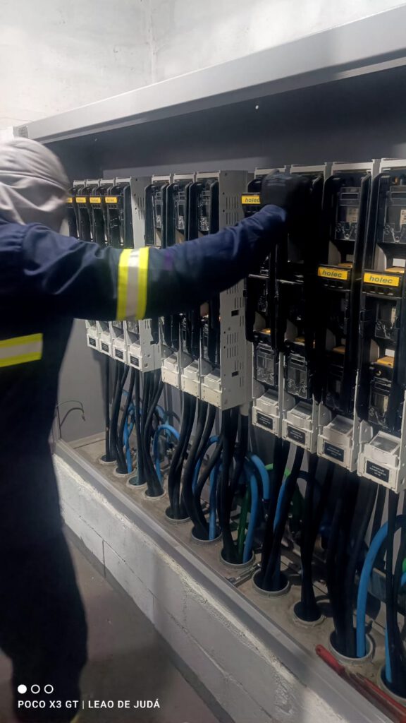 Técnico em EPI NR-10 inspecionando conexões e cabos do centro de medição